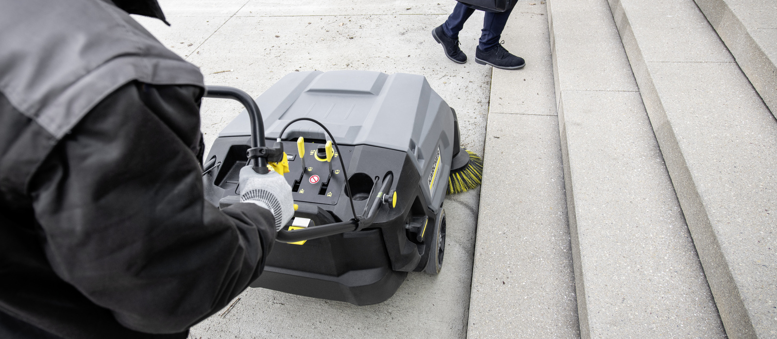 Cleaning the outdoor area with a walk-behind sweeper A person operating a Kärcher walk-behind sweeper