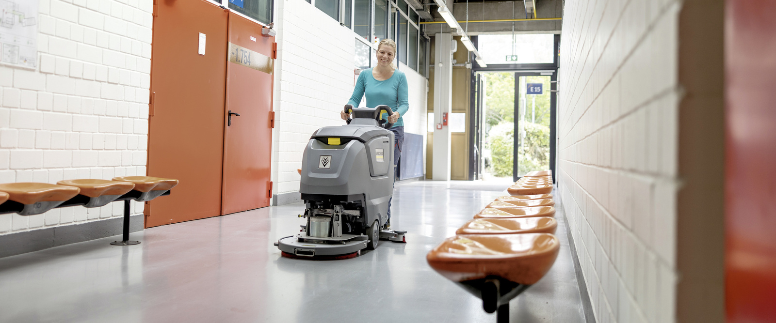 Eine Frau übernimmt die Innenreinigung im Flur mit einer handgeführten Scheuersaugmaschine