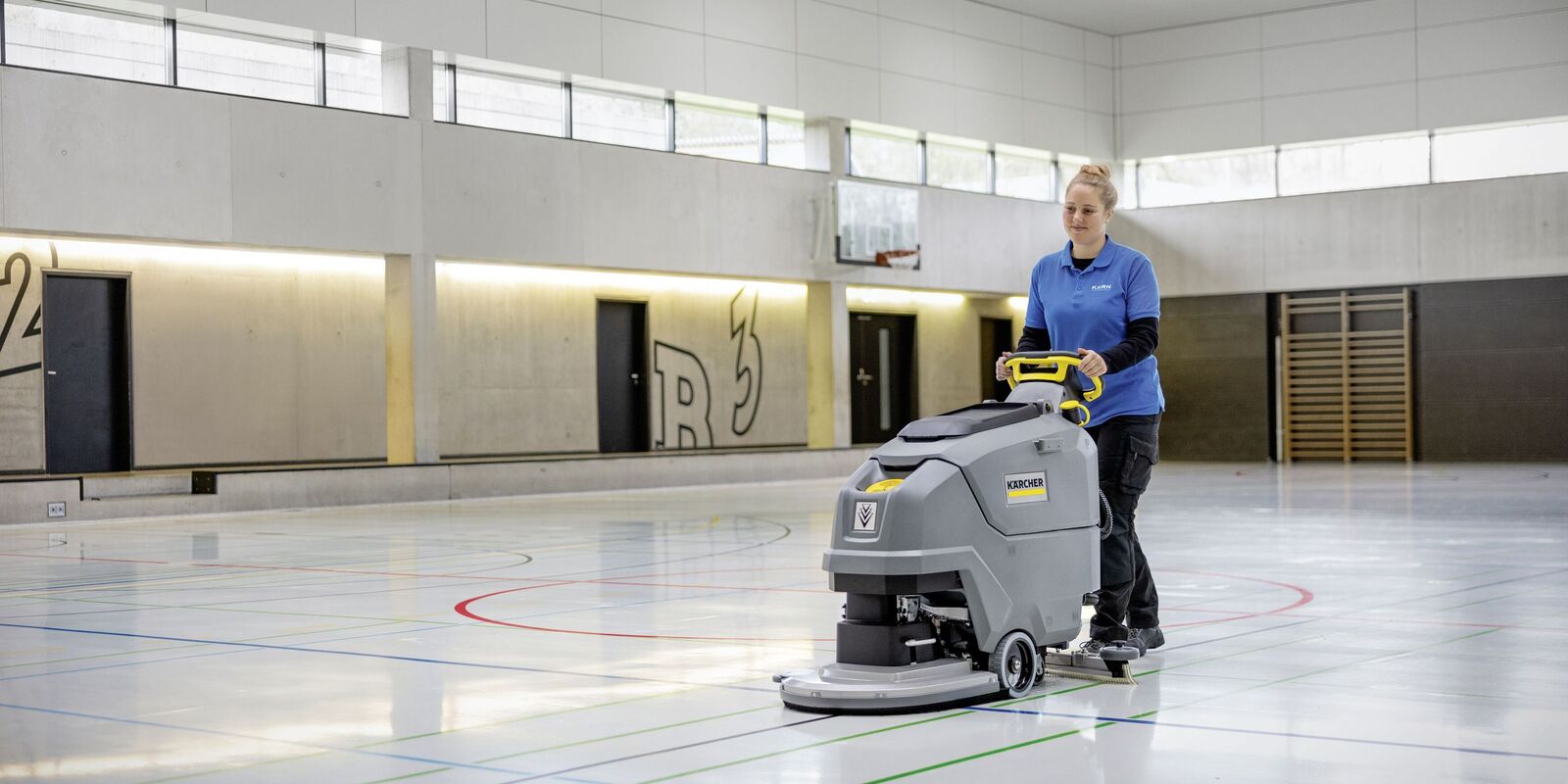 Eine Person reinigt den Boden in der Turnhalle mit der Scheuersaugmaschine