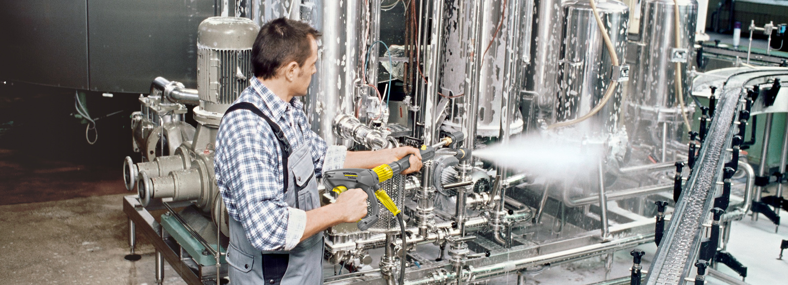 Pressure washer in use A man cleans the production area of a beverage industry with the help of a pressure washer