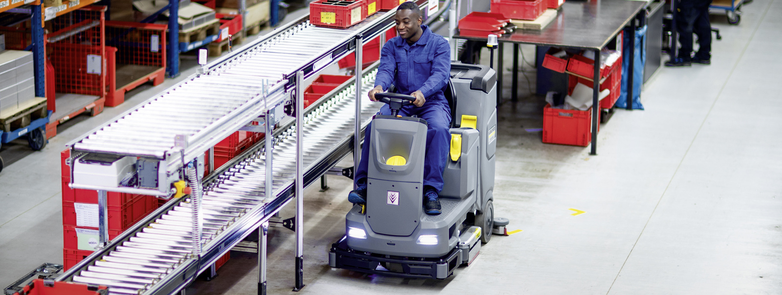 Ride-on scrubber dryer in use  A man cleans the floor with the ride-on scrubber dryer
