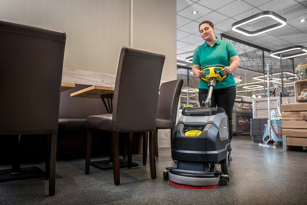 Compact Walk-Behind Floor Scrubbers A worker cleans floors in a grocery store cafe area.