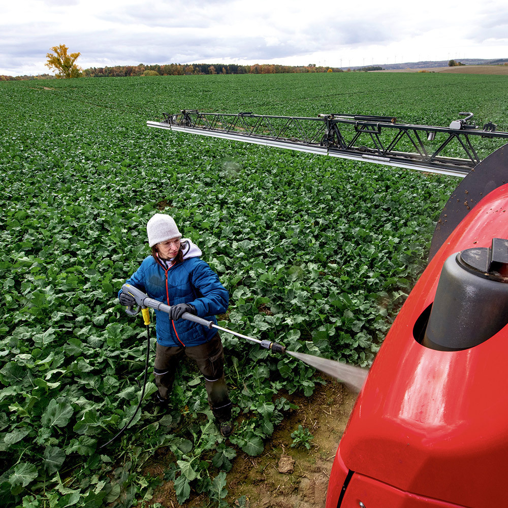 Cold Water Battery-Powered Pressure Washers A worker cleans agriculture equipment in the field