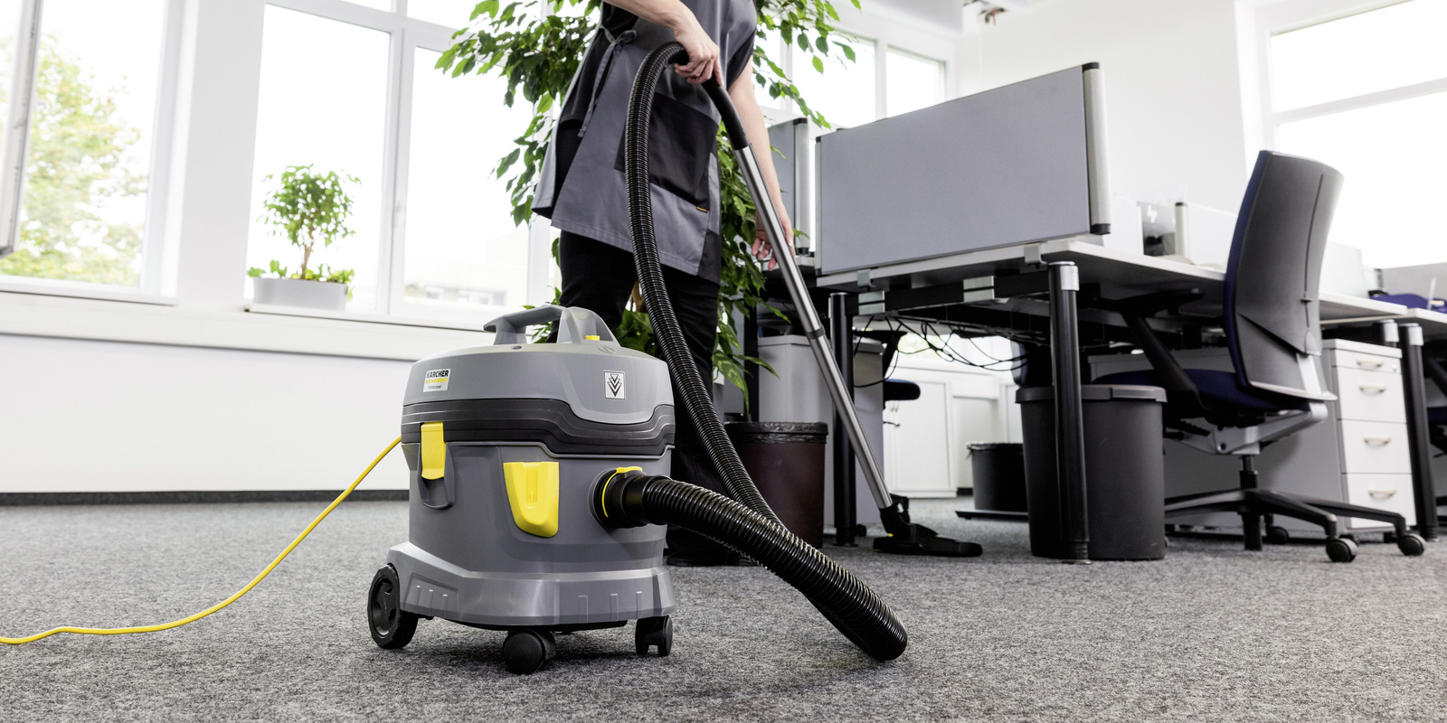 Office Cleaning A contract cleaner vacuums under an office desk with a Kärcher vacuum