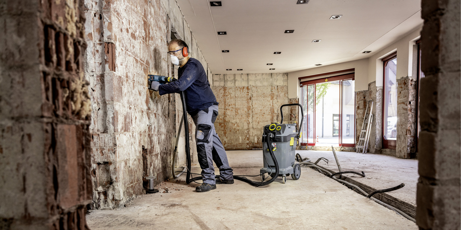 Baustaub entfernen ein Mann in Bauuniform reinigt eine Wand im Rohbau mit einem Sicherheitssauger