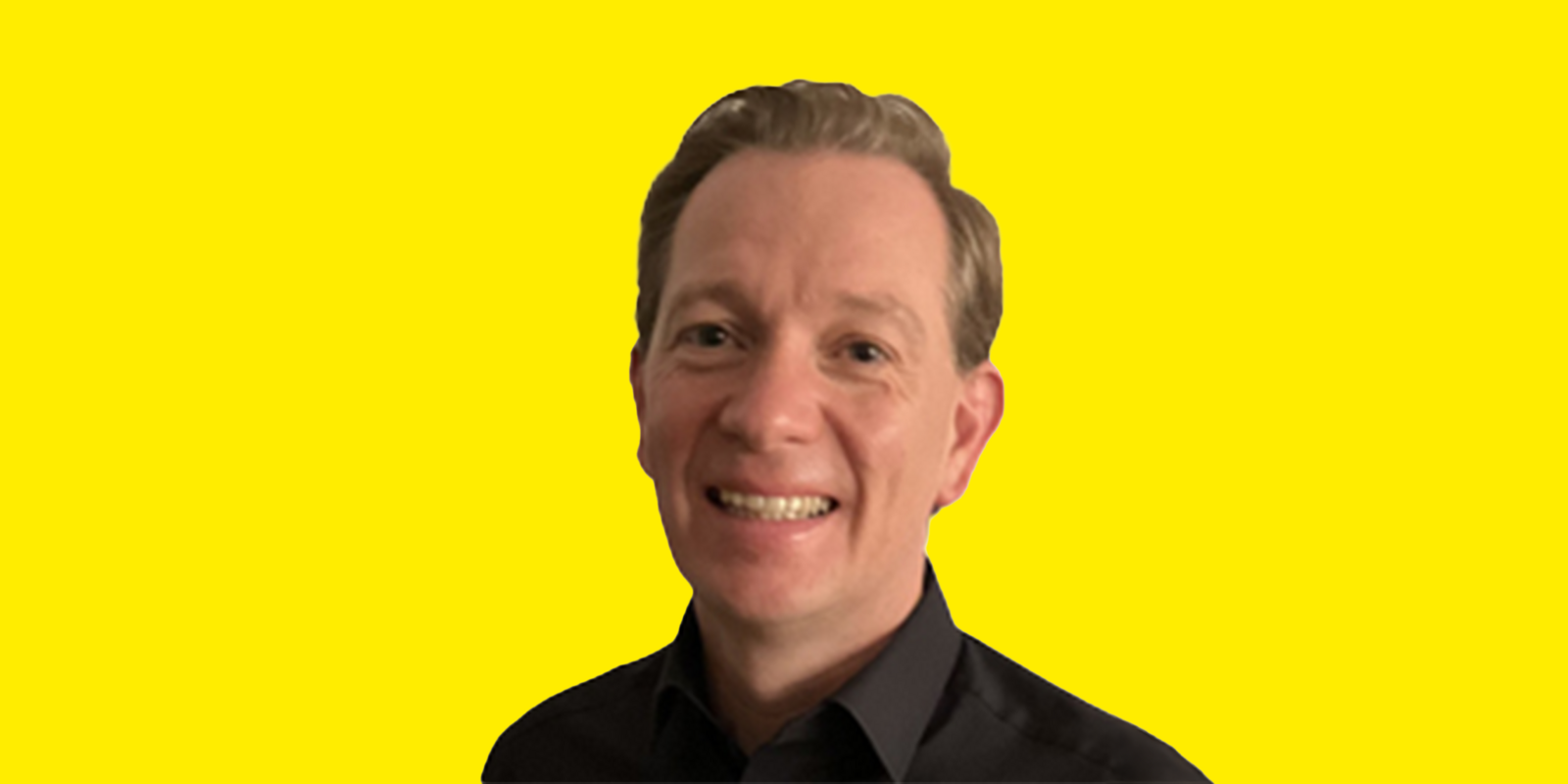 Clemens Burgstaller Das Bild zeigt Christian Burgstaller im Portrait, der in die Kamera blickt und breit lächelt. Er hat kurzes, hellbraunes Haar, das leicht nach hinten gestrichen ist. Er trägt ein dunkles Hemd. Der Hintergrund ist schlicht und gelb.