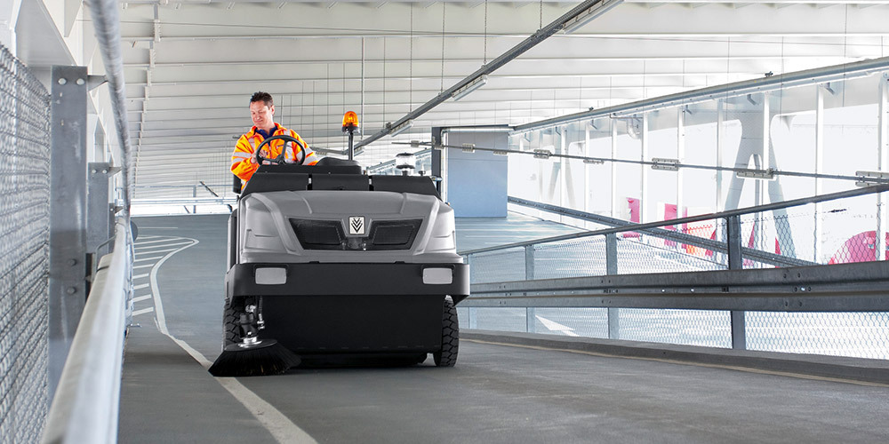 A man cleaning a stadium parking garage with a Kärcher ride-on sweeper