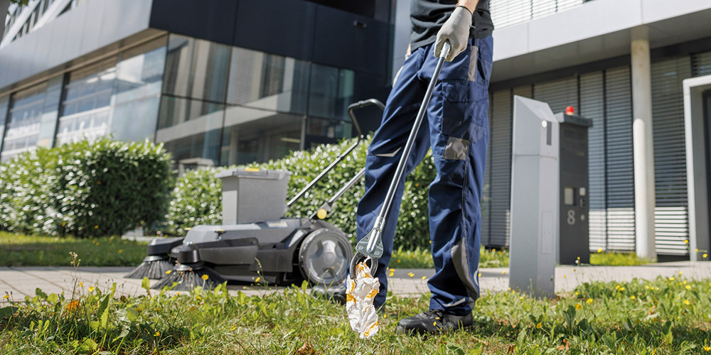A man cleans an outdoor area with a garbage grabbing tool