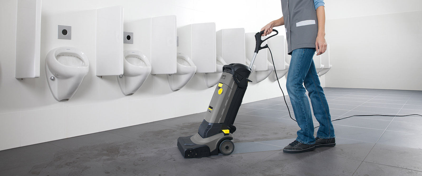 Cleaning Restrooms and Changing Rooms A worker cleans restroom floors using a compact walk-behind floor scrubber