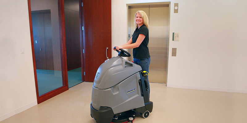 A worker operates safety and comfortably using a Chariot stand-on floor scrubber