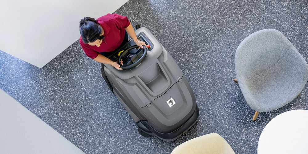 Overhead view of a worker cleaning carpets with a Karcher stand-on vacuum