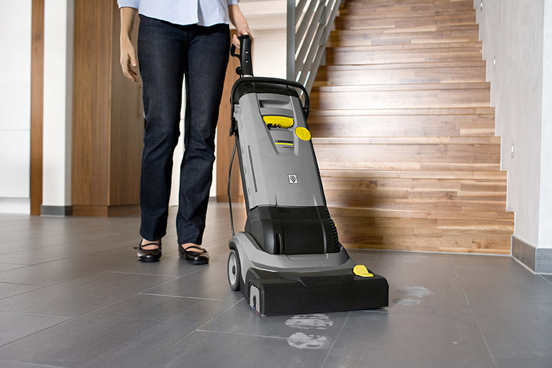 A worker cleans flooring with a floor scrubber