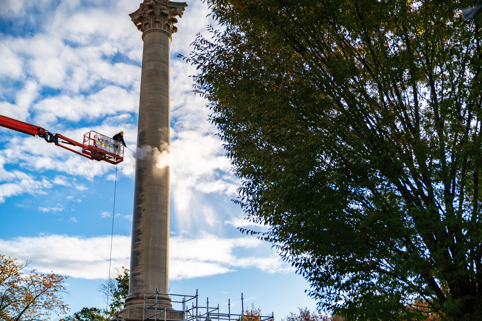 Wide Shot Of Man On Boom Lift Cleaning A Large Pillar With A Pressure Washer