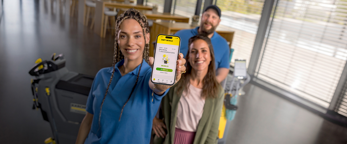 Connecten Sie Ihr Personal und Equipment mit Connected Cleaning Ein lächelndes Reinigungsteam mit Maschine und Roboter zeigt Connected Cleaning auf einem Handy