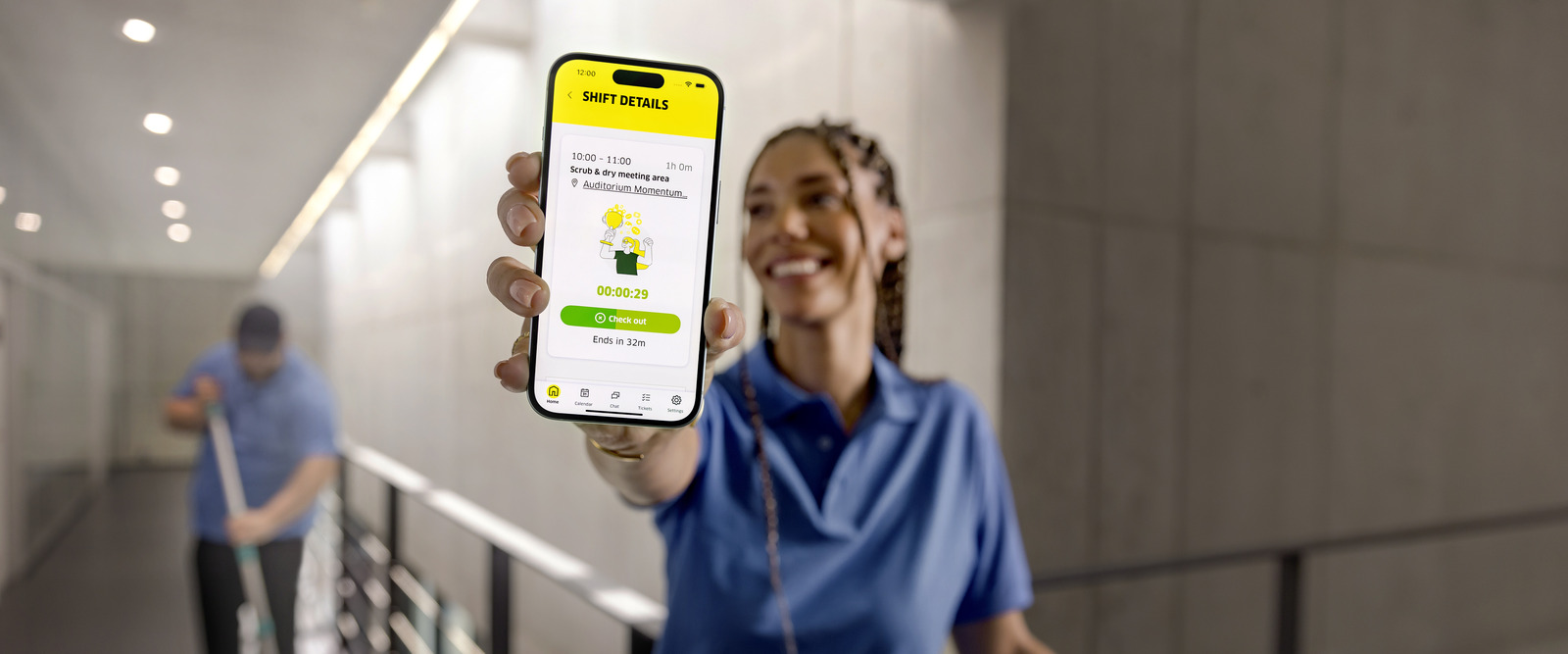 Connected Cleaning hilft Objektleiter dabei, mit der Arbeit ihres Teams verbunden zu bleiben. Eine lächelnde Reinigungskraft zeigt die Connected Cleaning Mobile App mit einer laufenden Schicht.