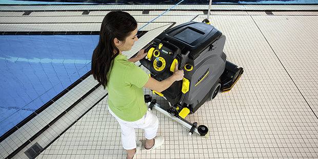 A worker cleans floors at a hotel pool using a Kärcher walk-behind floor scrubber