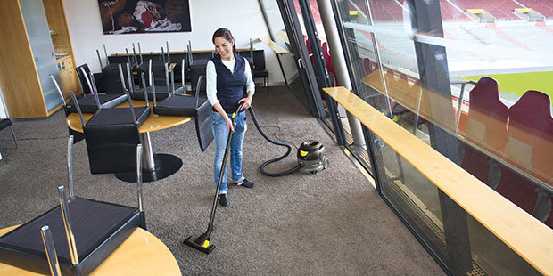 A worker cleans floors with a commercial canister vacuum cleaner