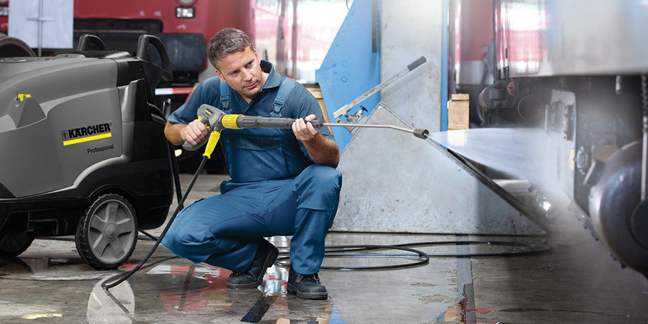 A worker cleans the underside of a big rig with a hot water pressure washer