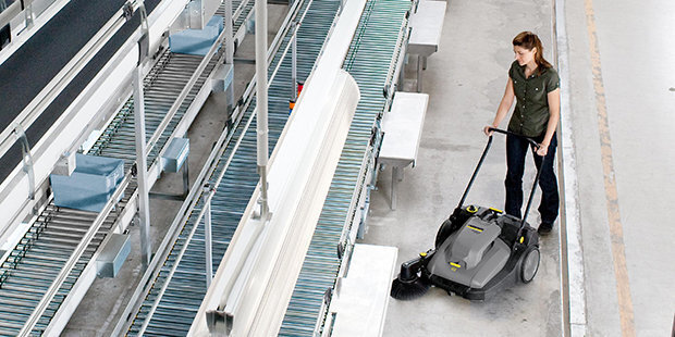 An aerial view of a worker sweeping floors in a manufacturing facility