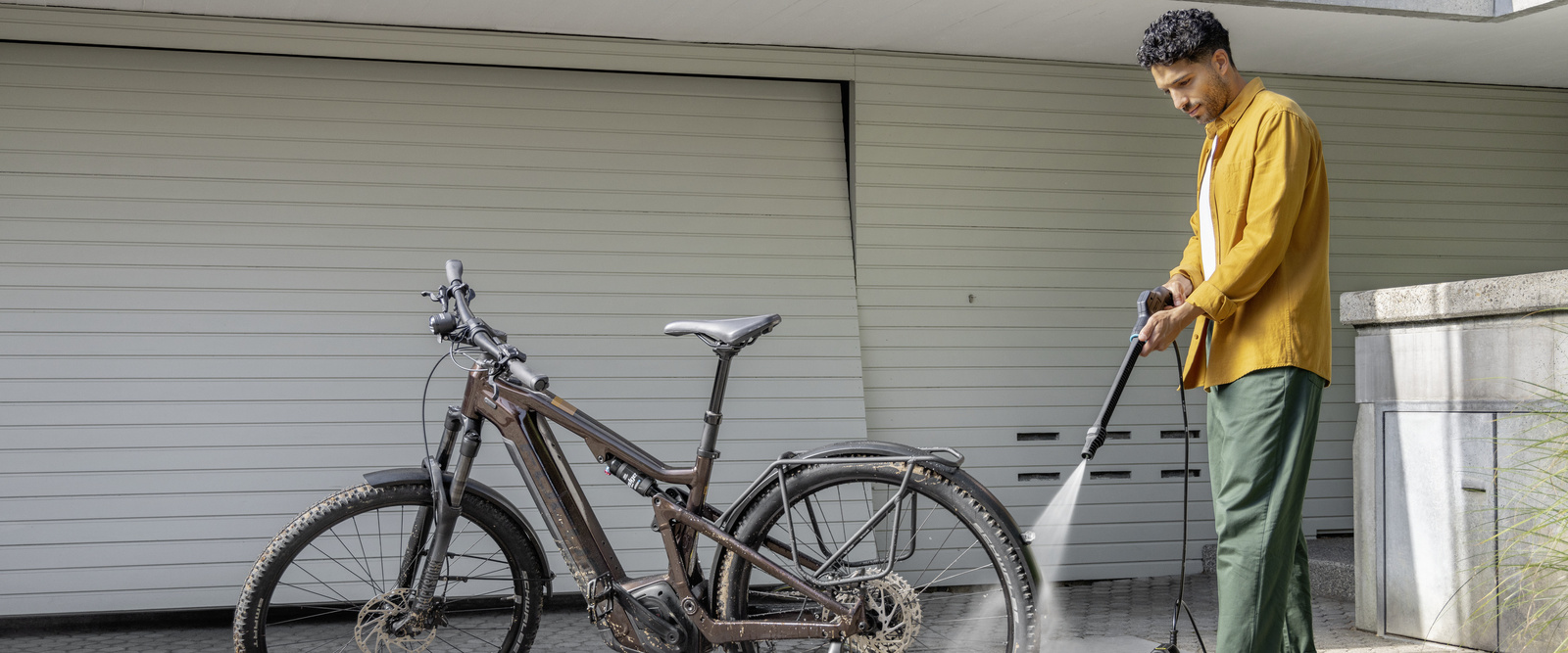 Žena čisti svoj bicikl ispred garaže Kärcherovim mobilnim vanjskim čistačem