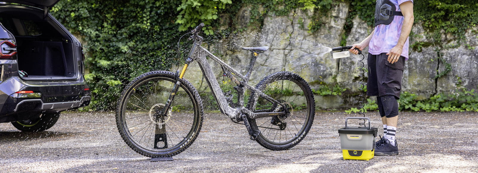 Žena čisti svoj cestovni bicikl pored stabla Kärcherovim mobilnim vanjskim čistačem