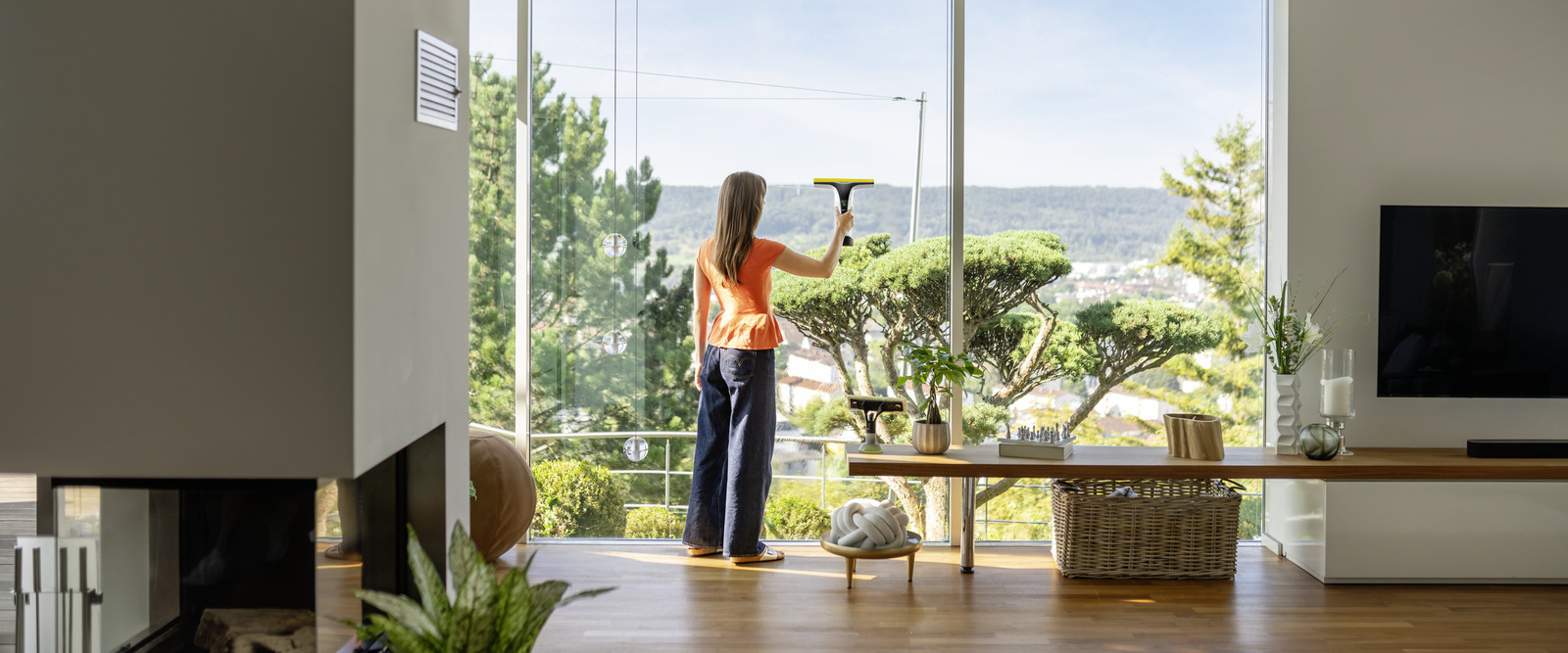 Frau reinigt Fenster mit einem Akku-Fensterreiniger von Kärcher.