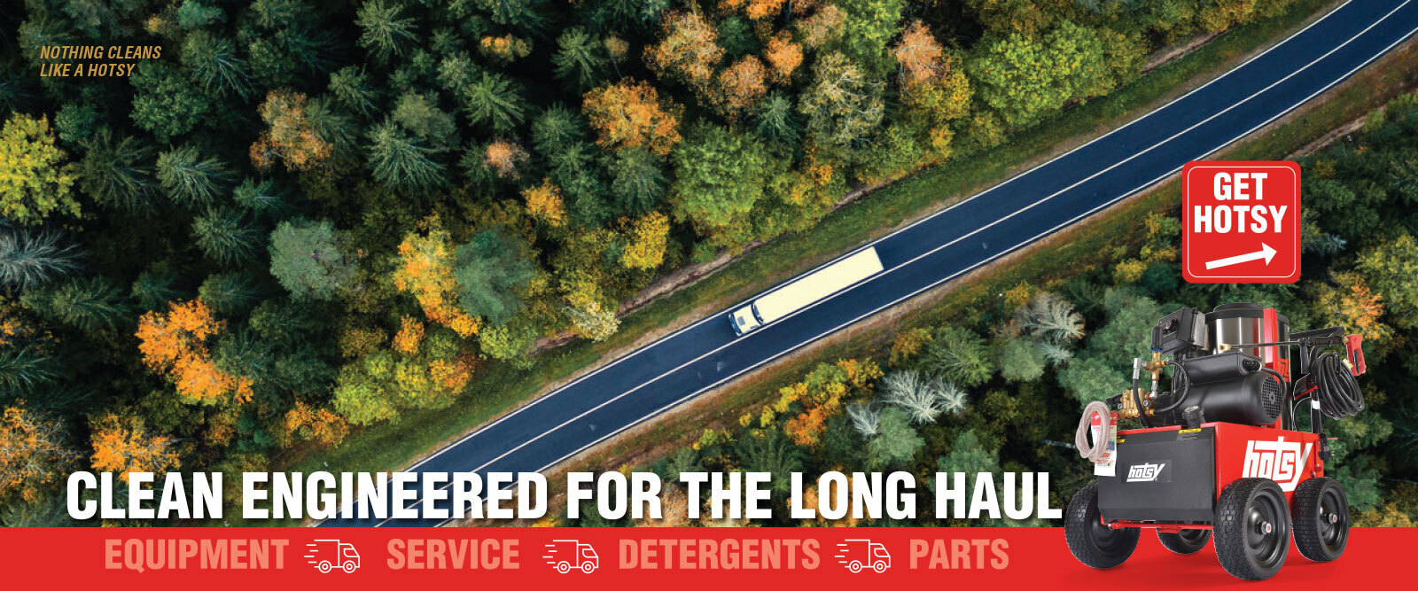 An aerial view of a semi-truck driving down a long stretch of road with trees on either side.
