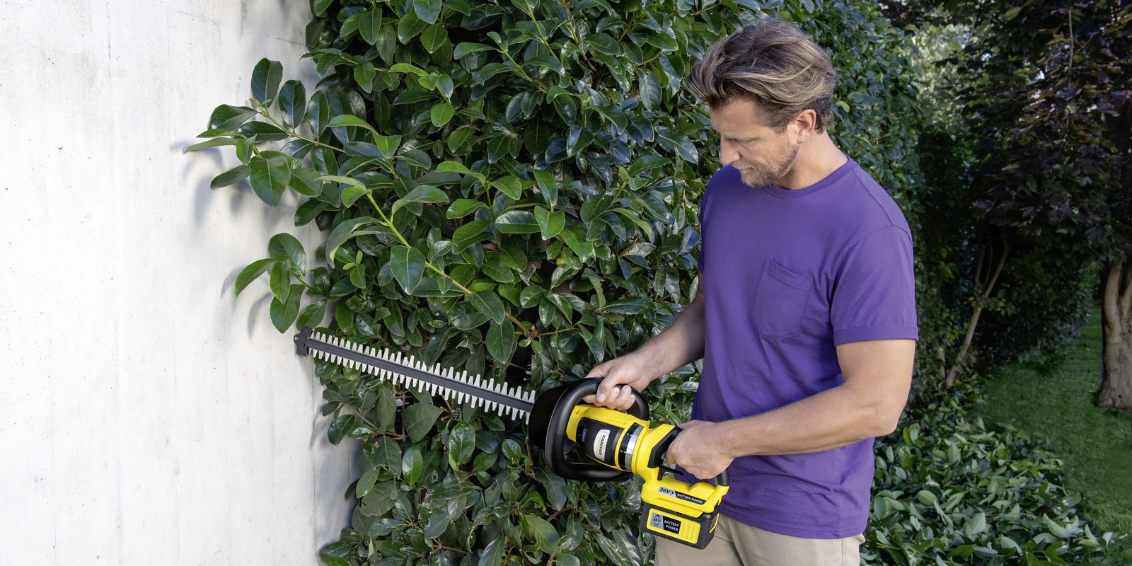 Messerspitzenschutz A man trims his hedge near a wall with the Kärcher battery hedge trimmer