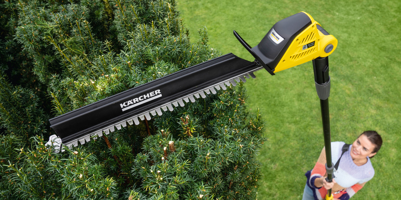Sawing fuction from above: A woman trims her hedge with the help of the Kärcher battery-powered pole hedge trimmer
