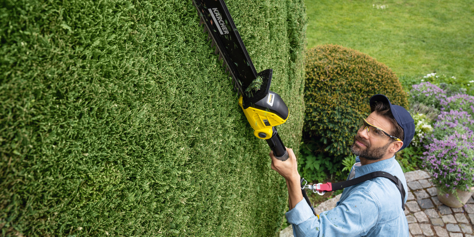 Shoulder belt A man works with the Kärcher battery hedge trimmer overhead and uses a shoulder belt
