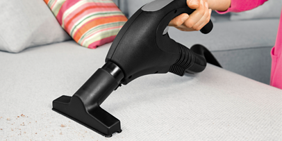 Woman cleaning the sofa using the steam vacuum cleaner's hand nozzle