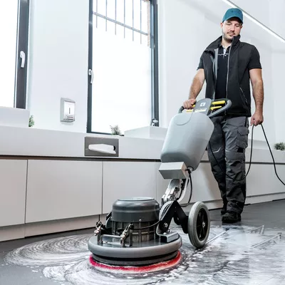 Man seen cleaning a linoleum floor using a corded Kärcher scrubber dryer.