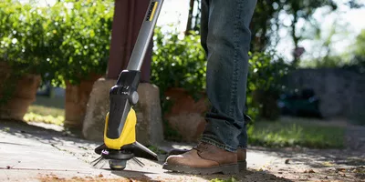 Person removes weeds on a stone terrace with the Kärcher cordless weed remover