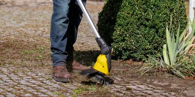 Person removes weeds between paving stones with the Kärcher cordless weed remover