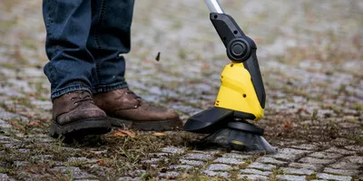 Person removes moss on stone patio with Kärcher cordless weed remover
