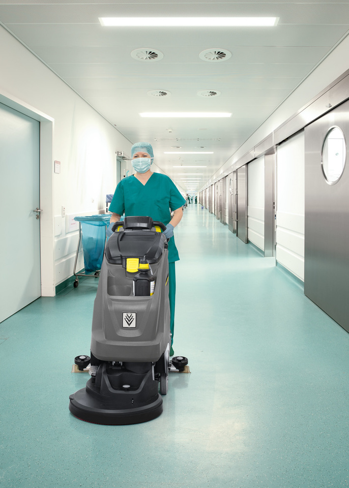 Desinfektion mit Scheuersaugmaschine Krankenhausangestellte in Schutzkleidung reinigt den Boden mit einer Scheuersaugmaschine