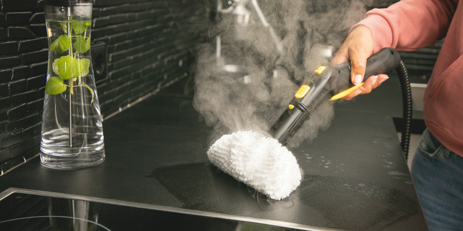 Person reinigt Küchenoberfläche mit Dampfreiniger mit Mikrofasertuch-Aufsatz
