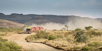 Abgebildet ist ein australischer Road Train LKW im Outback auf einer staubigen Straße.