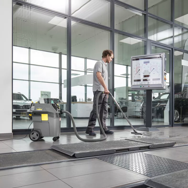 Bir kişi, otomobil bayisinde fayans zemin üzerinde Kärcher marka ıslak vakumlu temizleyici kullanıyor.