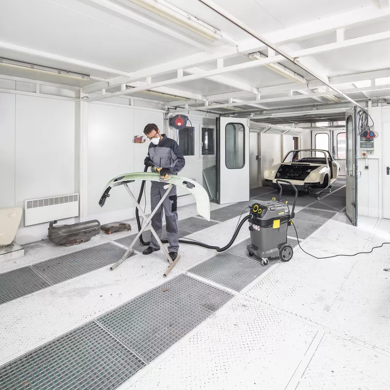 Bir kişi boya atölyesinde Kärcher marka emniyetli elektrikli süpürge kullanıyor.