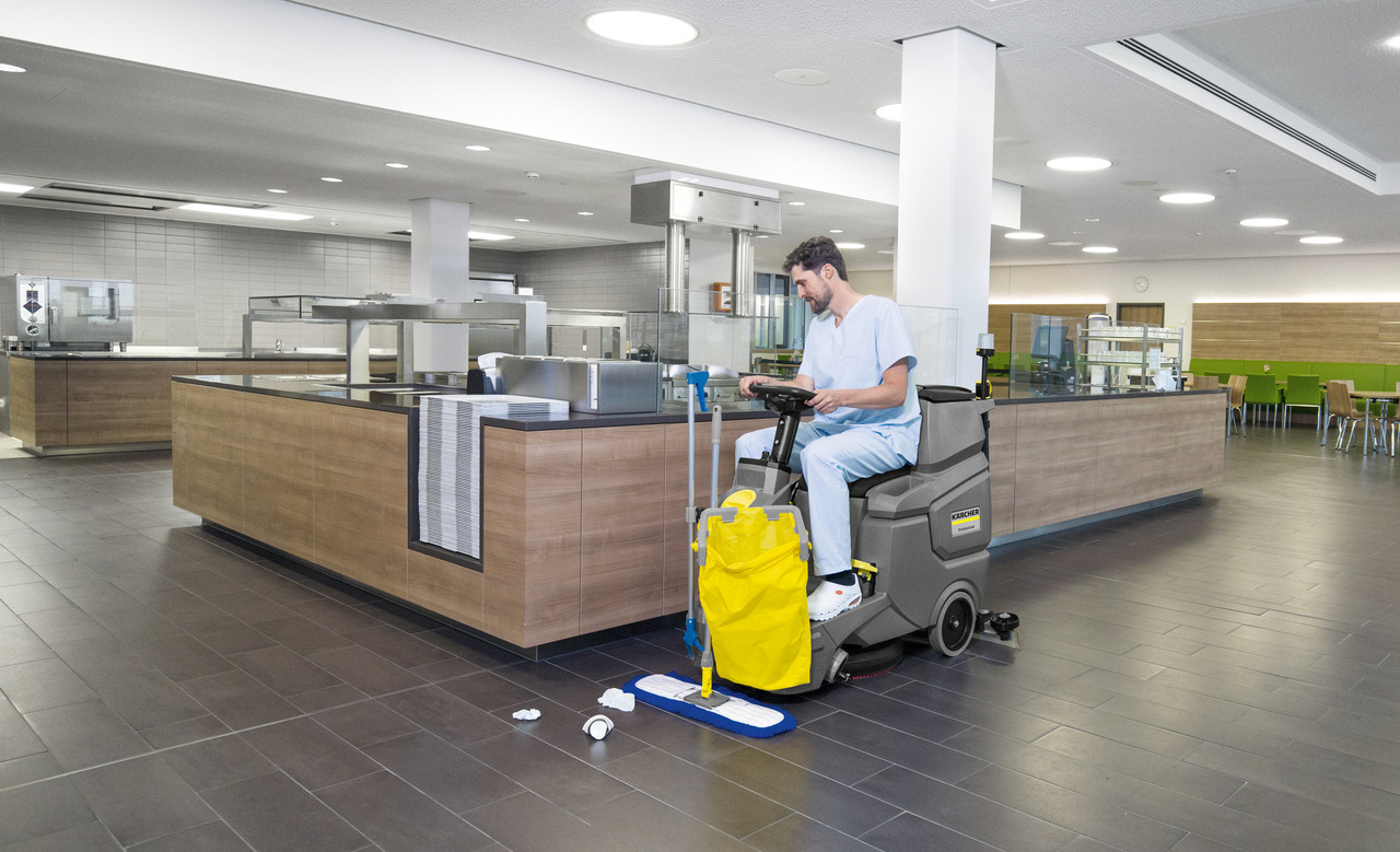 Ride-on floor scrubber used in a cafeteria Man scrubs a lunchroom floor using a Kärcher BD 50/70 R ride-on scrubber