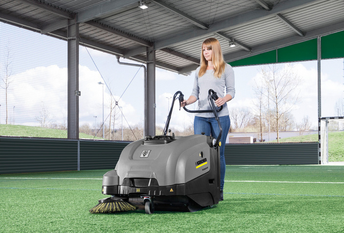 Walk-behind floor sweeper in use Woman cleans artificial turf using a walk-behind floor sweeper