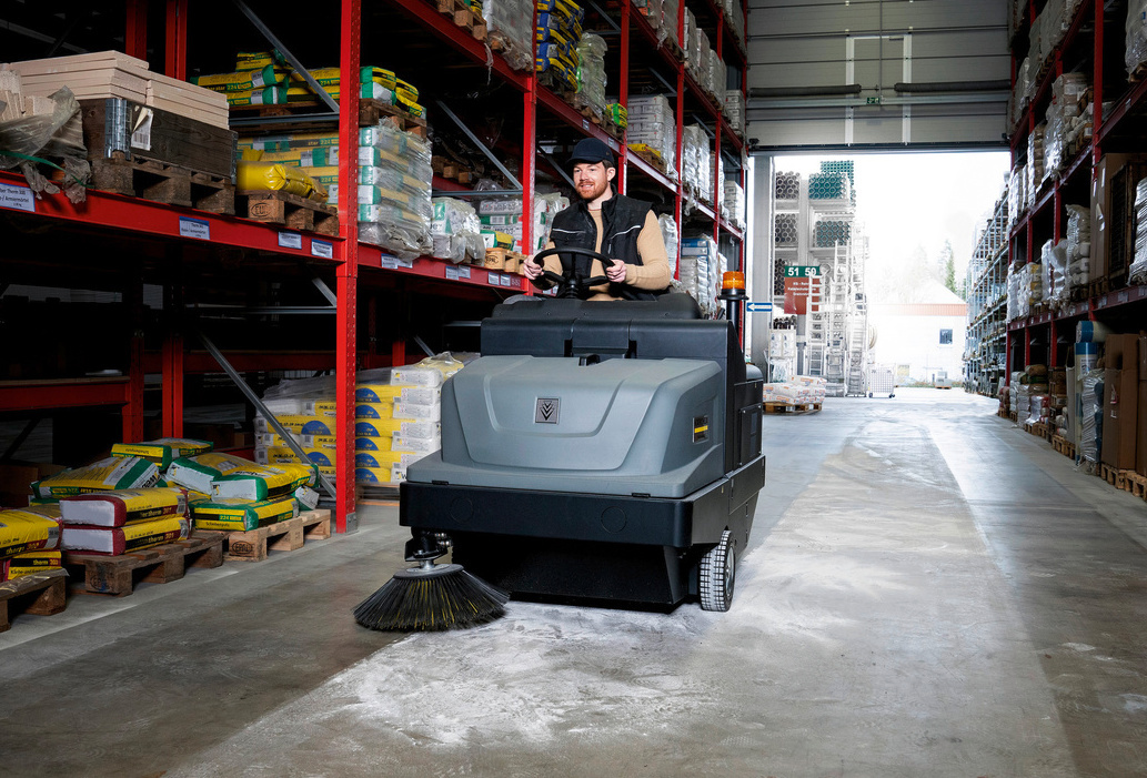 Ride-on floor sweeper in use Man cleans a warehouse floor using a Kärcher ride-on floor sweeper