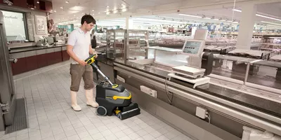 Person cleaning the floor in a supermarket using a Kärcher scrubber dryer
