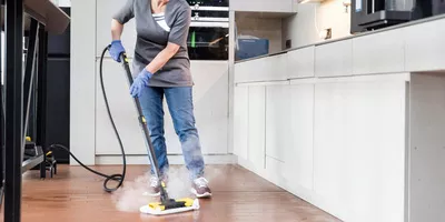 Person disinfecting a tiled floor in a kitchenette using a Kärcher steam cleaner